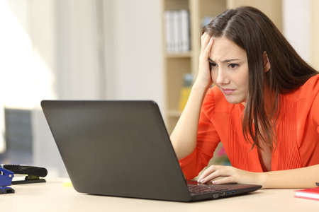 Sad and worried entrepreneur working on line with a laptop in an office desk or homeの写真素材