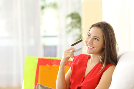 Woman thinking with credit card sitting on a couch with shopping bags at homeの写真素材