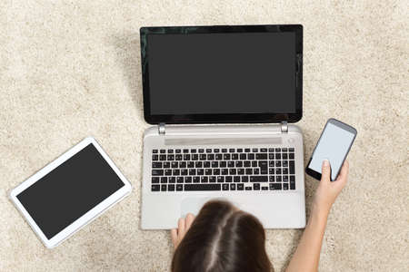 Woman working with multiple device screens lying on the floor at home
