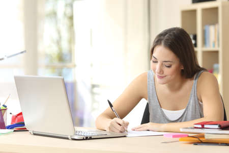 Beautiful student studying on line and learning writing notes in a desk at homeの写真素材