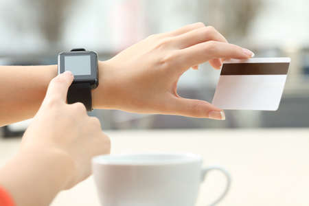 Close up of a girl hands buying on line with a credit card and a modern generic smart watch in a bar...