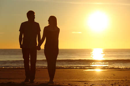 Front view of a full body of a couple silhouette walking together on the beach at sunset in summerの写真素材