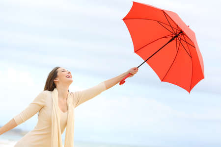 Playful girl joking with a red umbrella on the beach with the sky in the backgroundの写真素材