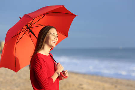 Portrait of a happy girl with red umbrella on the beach at sunset with the horizon and sea in the backgroundの写真素材