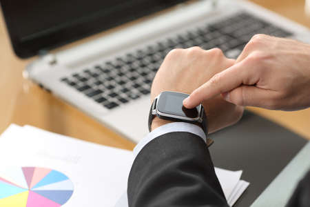 Businessman hands using a smart watch with the finger on the touch screen sitting in a desktop at office with a computer in the backgroundの写真素材