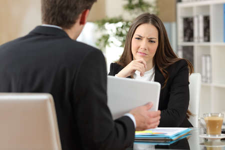 Salesman trying to convince a doubtful customer showing products in a tablet at workplace