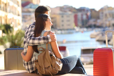 Couple of tourists sitting and cuddling while watching vacations destination in a port with colorful urban buildings in the backgroundの写真素材