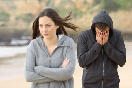 Teenager couple breaking up after argument. The angry girlfriend is rejecting her sad boyfriend