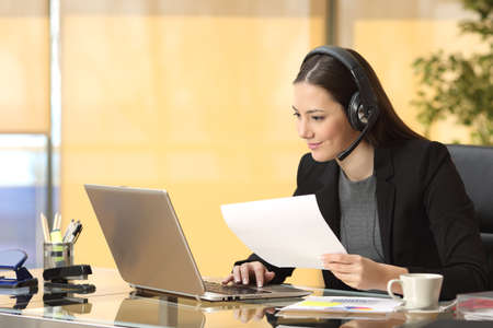 Freelance operator working online with a laptop and headsets and holding a document at office