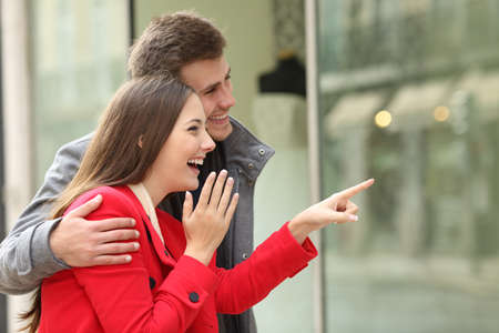 Excited fashion couple shopping and watching in a storefront in a town streetの写真素材
