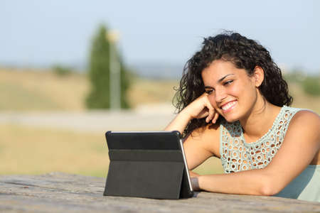 Happy girl watching videos in a tablet in a park outdoors