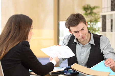 Incompetent businessman with disordered desktop attending an upset client giving her a dirty report at officeの写真素材