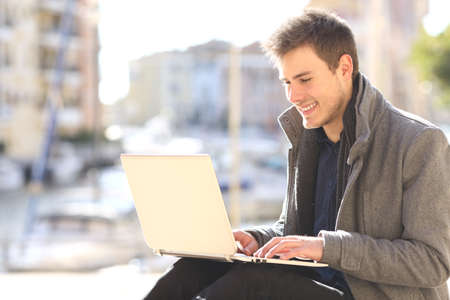 Elegant fashion entrepreneur working with a laptop outdoors sitting in the street of a port urbanization in winterの写真素材