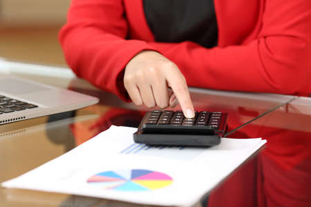 Closeup of a businesswoman hands accounting with calculator sitting in a desktop at office with her red suit in the backgroundの写真素材