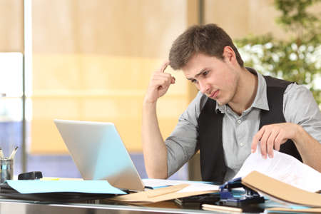 Incompetent businessman thinking how to do his job online with messy desk at officeの写真素材