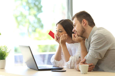 Frustrated buyers trying to pay online with credit card and a laptop at homeの写真素材