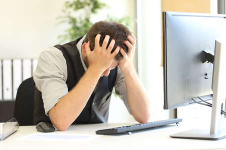Depressed businessman after bankruptcy lamenting with hands on the head in a desktop in the office