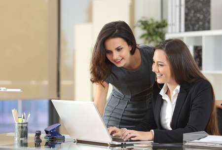 Two happy businesswomen coworking with a laptop in a desktop at officeの写真素材