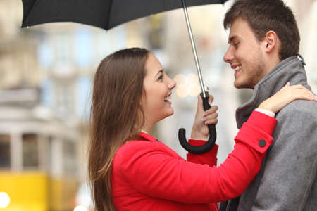 Side view of a couple encounter in the street under an umbrella in a rainy dayの写真素材