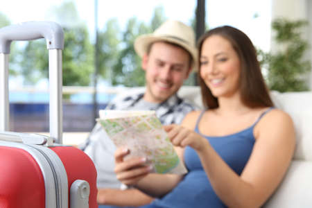 Couple of tourists searching location in a map during vacations sitting on a couch of an hotel or apartmentの写真素材