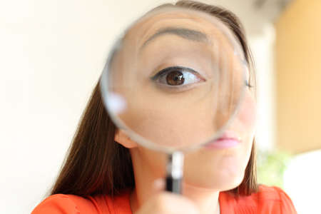 Front view close up of a suspicious businesswoman eye watching you with a magnifying glass