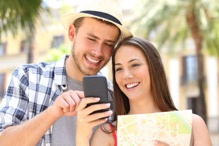 Tourists checking gps on a smart phone in the street of a touristic place on summer vacations with palm trees and buildings in the backgroundの写真素材