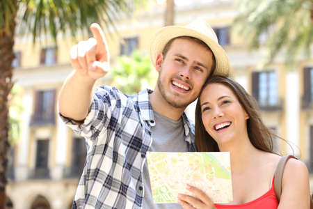 Couple of tourists consulting a guide map in the street of a touristic place during vacations with buildings and palm trees in the backgroundの写真素材