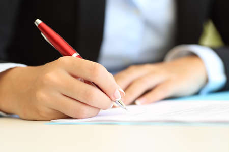 Close up of a businesswoman hands writing in a document on a desktop at officeの写真素材