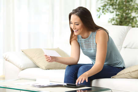 Housewife calculating accounting holding a receipt sitting on a sofa in the living room at homeの写真素材