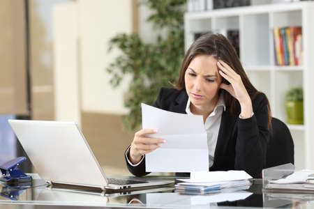 Worried businesswoman reading a notification sitting in a desktop at officeの写真素材