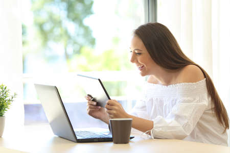Funny girl watching media content on line in a tablet sitting in a table near a window with a warm green background outdoorの写真素材