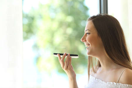 Portrait of a girl using the voice recognition of the phone and looking through a window of a house