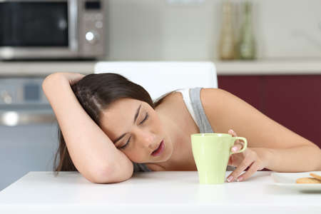 Tired girl sleeping on the table of the kitchen at breakfastの写真素材