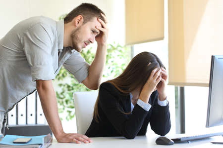 Two worried coworkers with a desktop computer lamenting after a great mistake at officeの写真素材