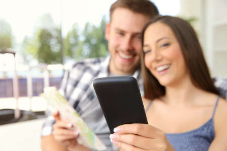 Couple of tourists searching location in a phone during vacations in an hotel or apartment with a window in the backgroundの写真素材