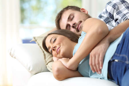 Couple hugging and sleeping in a comfortable couch in the living room at homeの写真素材