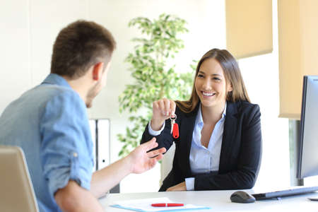 Happy real estate agent giving house keys to a customer after signing contract in the officeの写真素材