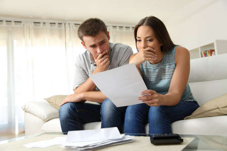 Worried couple reading a letter sitting on a couch in the living room at homeの写真素材