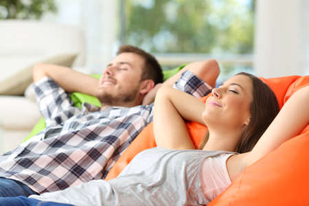 Couple or roommates relaxing lying on comfortable poufs in the living room at homeの写真素材