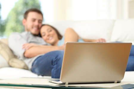 Couple watching tv in a laptop lying on a couch at homeの写真素材