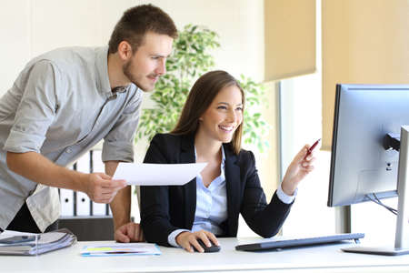 Businesspeople co-working comparing a desktop computer information with paper document at officeの写真素材