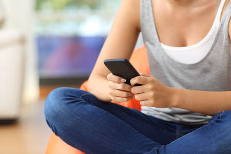 Teen hands using a smart phone sitting on a pouf at homeの写真素材