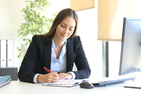 Busy businesswoman writing in an agenda on a desktop at officeの写真素材