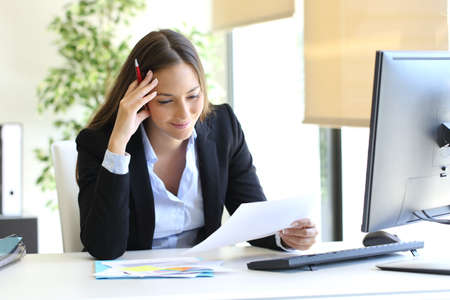Businesswoman reading a document sitting in a desktop at officeの写真素材