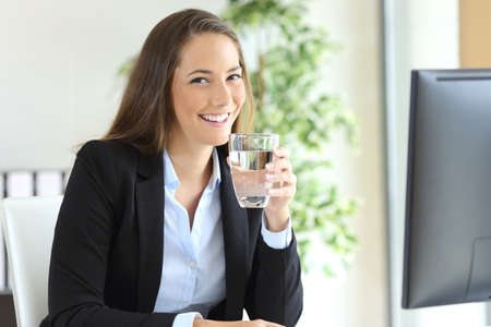 Businesswoman wearing suit  holding a water glass in a desk and looking at camera at office