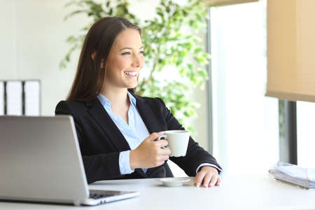 Pensive executive drinking coffee and looking through a window at officeの写真素材