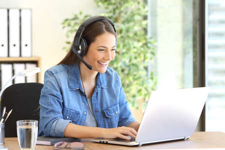 Freelance operator working in telemarketing on line with headsets and a laptop in a desktop at officeの写真素材
