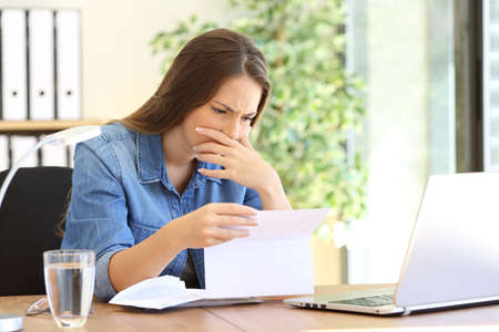 Worried entrepreneur girl working at office reading bad news in a letter on a desktopの写真素材