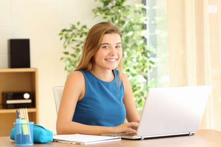 Confident student posing looking at camera while doing homework sitting in a desk at homeの写真素材