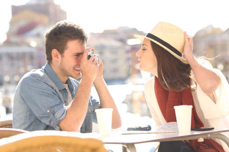 Side view of a tourist joking and photographing his girlfriend in a hotel terrace during summer holidaysの写真素材